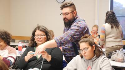 A classroom of students working on a project. An instructor helps a student.