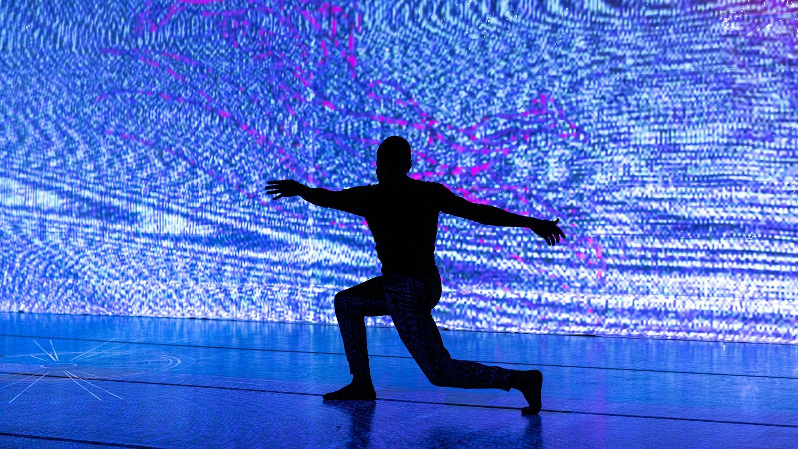 Person silhouetted in a lunge pose before a large blue and purple abstract digital display.