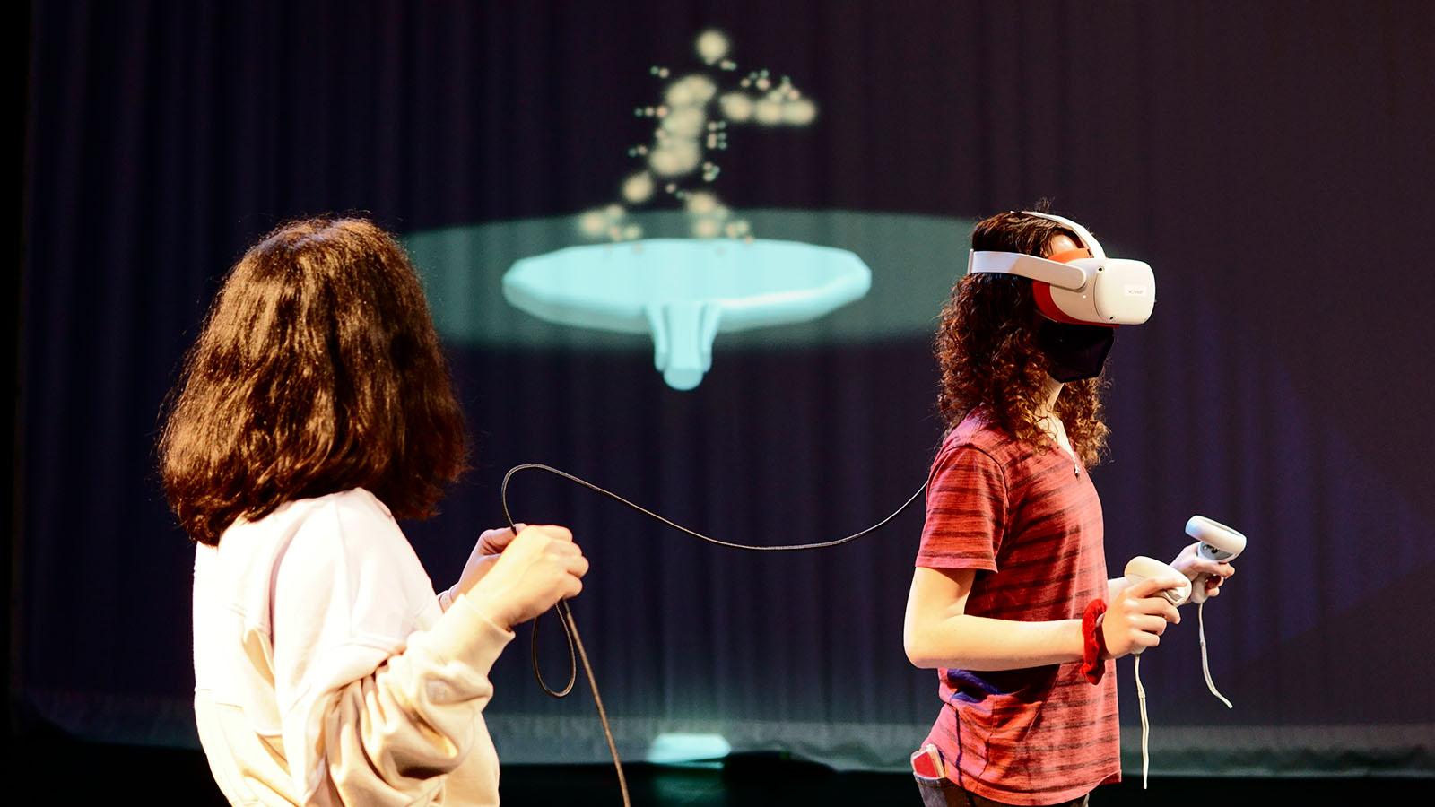 Two people engage in a VR experience with a projection in the background