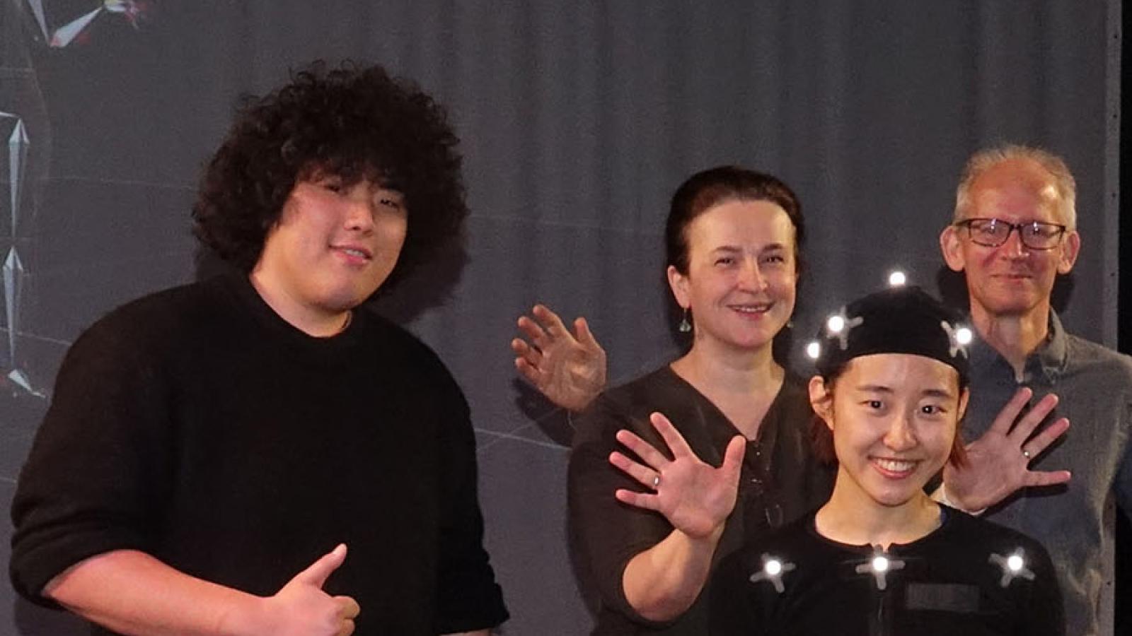 An asian woman smiles in a motion capture suit covered in retroreflective dots while the project team smiling around her 